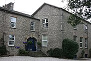 Large grey stone two-story building with a short staircase up to a blue entrance door,