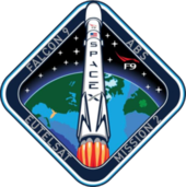 A diamond-shaped emblem with blue borders encasing an artistic depiction of a Falcon 9 rocket launching to space.