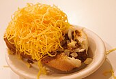small oval white plate with cheese coney showing bun, hot dog, sauce, and shredded cheese