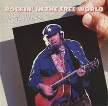 A photo of a man holding the photograph from the album cover to Freedom: Young is playing guitar and singing in a blue outfit