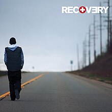 The cover features Eminem walking down the road under clear albeit cold looking blue sky. On top-right corner, in bold and capitalised format, the title RECOVERY appears.