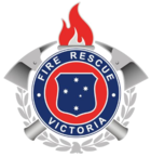 From a small silhouette of a brass firefighter's helmet rises a laurel wreath. Above it sits a shield of the Southern Cross, as in the Victorian coat of arms, encircled by the words FIRE RESCUE VICTORIA; behind this two crossed axes. A flaming torch surmounts the badge.