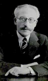 black and white photograph of elderly white man with white hair and grey moustache, bespectacled