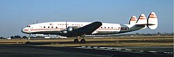 A large piston engined airliner taxiing past some large bomber aircraft