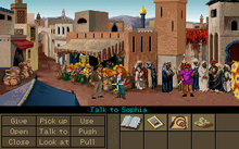 A video game screenshot showing the two protagonists in the middle of a crowded marketplace. The lower part of the image shows a variety of objects on the right side and a number of verbs such as "Pick up", "Use" and "Talk to" on the left side. The mouse cursor is pointing at Sophia, making the current command "Talk to Sophia".