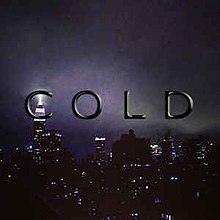 Black, shining text displaying the word "Cold" in front of a city during nighttime with grey clouds and lit buildings