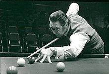 A man with round spectacles playing snooker