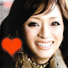 A up-close shot of Ayumi Hamasaki smiling and looking into the camera. On the lower left is a red heart.