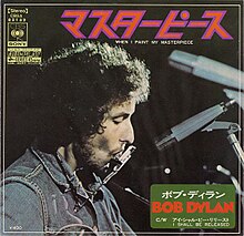 The Japanese single cover for Bob Dylan's 1971 single 'When I Paint My Masterpiece', b/w 'I Shall Be Released'. An image of Dylan performing live is the main design, specifically a close-up of his head playing a harmonica next to a row of microphones, with the A-side identified in large Japanese text above him. The song is identified in English just below it. In the bottom right corner, the artist and B-side are identified in both Japanese and English on a dark green box. A variety of logos are printed in yellow in the upper left corner.
