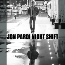A black-and-white image of Pardi walking down a sidewalk at night with his reflection in a puddle of water. Both the artist's name and song title are in between them, colored black.