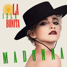 A blond woman in a black, bolero hat looking to the camera. The song and artist name are printed in red, yellow and green font on top of the image.