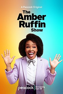 This official promotional poster depicts star Amber Ruffin in a pastel pink blazer, plum colored pants, and a white button up top with a plum bow tied at the neck. Ruffin is smiling, with her hands splayed on either side of her.