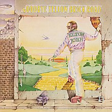 A wall with a worn poster showing a yellow brick road winding down towards the green plains and the sunset. Elton John, shown with a purple jacket bearing his name, has his right foot on the yellow brick road and his right hand holding on to the poster. On the sidewalk, a miniature piano with a musical note. The album's title is placed above the poster.