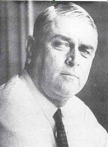 A black-and-white photo of a man in his fifties wearing a white shirt and black tie