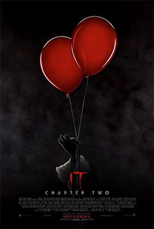 In a very dark foggy background, a hand of Pennywise the Clown holds two red balloons with two fingers.