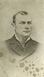 A gentleman posing for a photo in a suit and tie, seen from the chest up