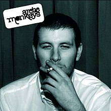A man smoking a cigarette in a blue-tinted black and white photo. The band name is in the upper left corner.