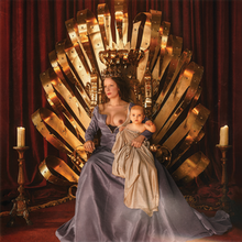 Halsey wears a blue-gray dress while sitting on a gold throne. A baby draped in beige cloth sits on Halsey's lap.