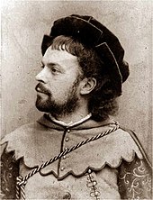 head and shoulders photograph of young man with neat moustache and beard in mediaeval costume