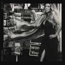 Mariah Carey poses in a black gown, surrounded by several posters, one of which reads "With You"