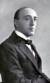 middle-aged white man, clean-shaven, with dark, receding hair, dressed in a suit and bowtie