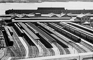 Black & white picture showing station facility with passenger cars. Hudson river visible behind the station.
