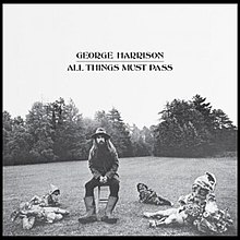 a black and white photo of George Harrison sitting on a stool surrounded by garden gnomes.