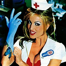A buxom nurse putting on a blue surgical glove with a seductive look in her eyes.