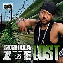 The cover features a man wearing a black tank top and hat, posing next to a green metal fence with barbed wire on top. Both the artist's name and song title appear below him, colored in white and green respectively.