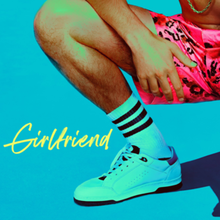 A crouched man wearing pink leopard-print shorts and white tube socks and shoes crouched in front of a solid blue background. To his right stands the title, "Girlfriend".