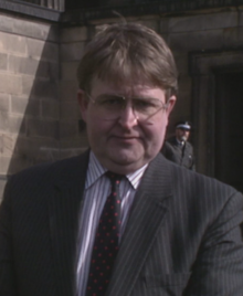 MacKay standing on a street, wearing a suit