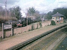 Deserted railway platform, with a steam locomotive pulling goods wagons in the background