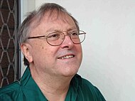 A man with the shot focused on his head. He is facing to the right and is wearing a pair of glasses and a green top.