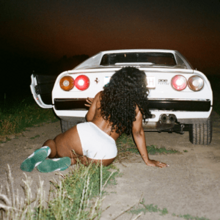 Cover art for "Snooze": SZA in white shorts, sitting on the ground in front of a white car's trunk