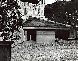 A black and white photo of a small triangular doghouse with a door on its left