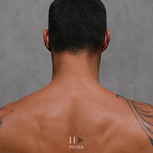 A back view of a person's back with a tatto. A pause and play symbol is seen at the bottom, with the play icon in Black and the album title "Pausa" (Spanish for "Pause") in white text.