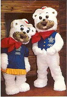 Two polar bear mascots with fuzzy white fur. The female is wearing a blue dress, and the male a blue vest. They each wear a red bandana and cowboy hat.