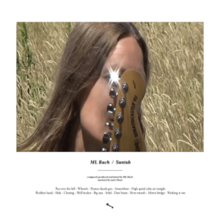 Buch's face obscured by the headstock of a guitar, with a gleam of light shining off a tuning peg over her eye, in front of a field