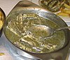 Eel meat in a green herb sauce in a metal serving dish.