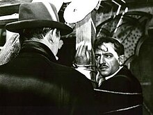 A screen capture from the film, showing a distraught César tied up to a pole staring at Tony le Stéphanois, who has his back to the camera.