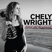 A black-and-white image of a woman standing on a seashore, holding an acoustic guitar over her right shoulder. The text "Chely Wright" and "Lifted Off the Ground" appear on the right side of the image over the water.