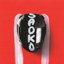 On a red background, a black motorcycle helmet (it's shield down) with pink hair attached outwards, forming bunches. The song's title "SAOKO" is painted in white vertically on the helmet with the artist's name, Rosalía, printed on the bottom part of the "O".