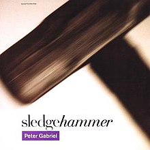 An blurred image of a sledgehammer. The text reading "hammer" in the song's title is seen italicized, while the artist names appear in white text in a purple rectangle.