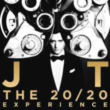 Black and white image on a black background. A blurred man is shown, wearing a suit and bowtie, looking at the camera from afar. In front of him is a phoropter and golden text reading "JT" and "THE 20/20 EXPERIENCE".