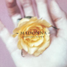 An orange flower is held in the palm of a white hand in front of a purple background with the artist and the song name written on top of it.