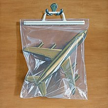 A bag with a gold plane inside hanging from a hook on a wooden background