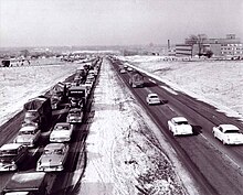 A black-and-white photo shows a four-lane freeway divided by a grass median. In the oncoming lanes, traffic is congested into the distance. With few exceptions, the 401 is surrounded by farmland.
