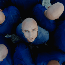 The cover artwork for "Hollow". The cover features Dons in a blue outfit looking up, surrounded by others with the same outfit as him.