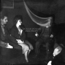 A black-and-white photo of a man seated with a whispy smear stretching from his face and two onlookers seated to his side