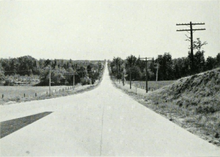 Black and white photo of a concrete two-lane road stretching straight towards the distant horizon